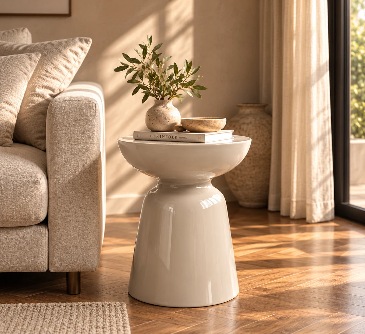 Table d'appoint Calice grège brillant à côté d'un canapé beige, avec un vase, une coupe et des livres